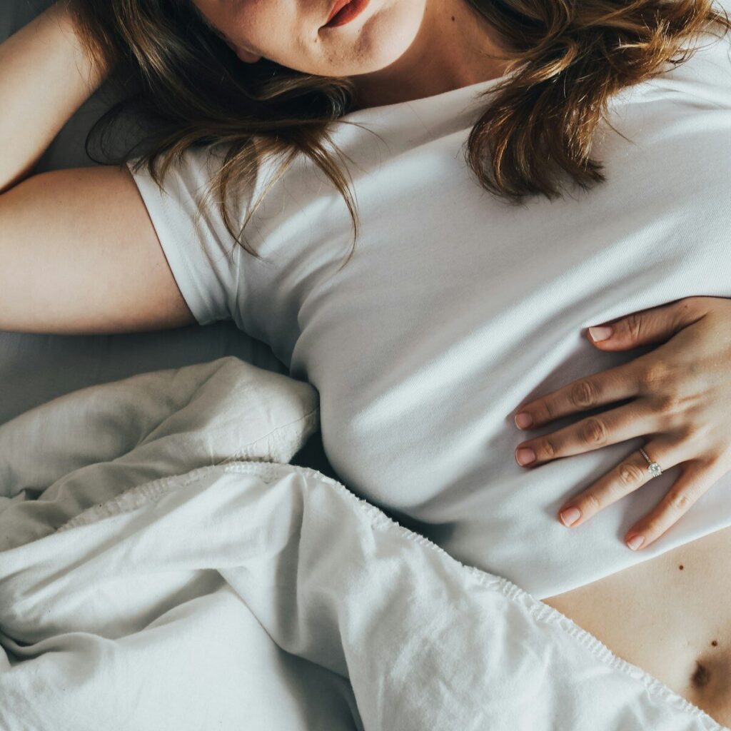 une femme allongée dans un lit avec une main sur son ventre illustrant des troubles digestifs liés à la consommation de produits glacés