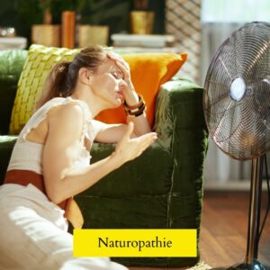 Une femme épuisée se tient devant un ventillateur, illustrant les difficultés physiques causées par la canicule